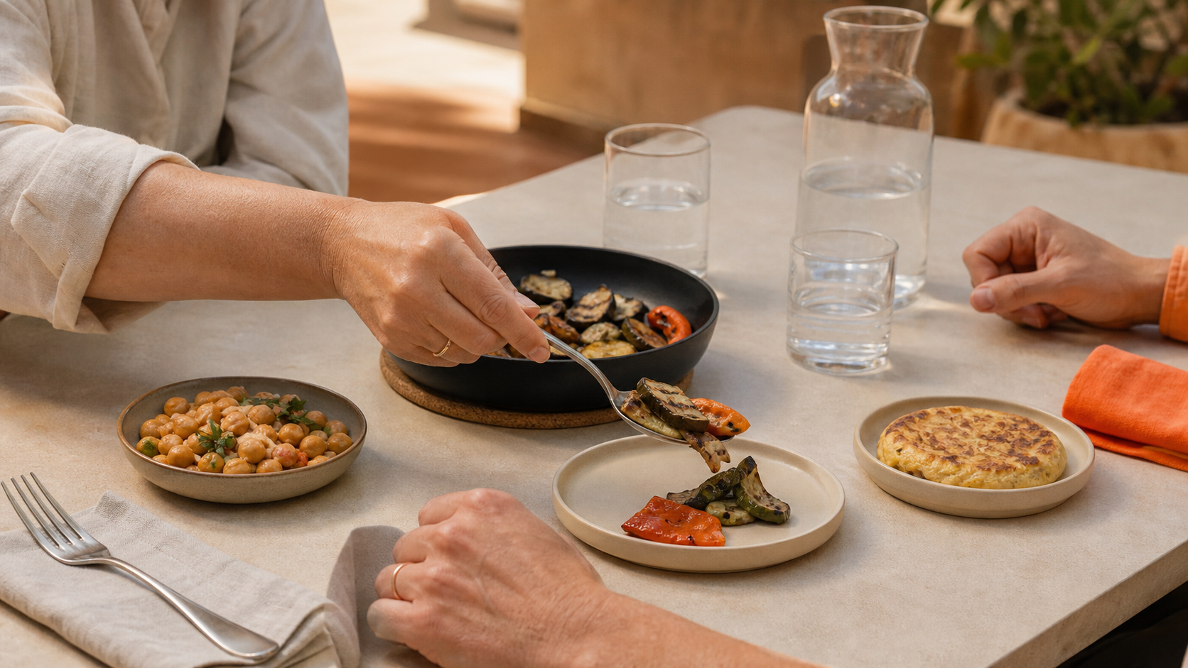 Manos compartiendo tapas en una terraza mientras una persona se sirve verduras en su plato.